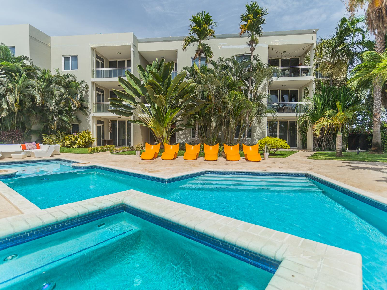 Captivating Pool Area of the Apartment in Oranjestad Aruba - A spot for friends and family to gather and socialize - Palm trees and tropical plants enhance the vacation feel - Modern beach chairs