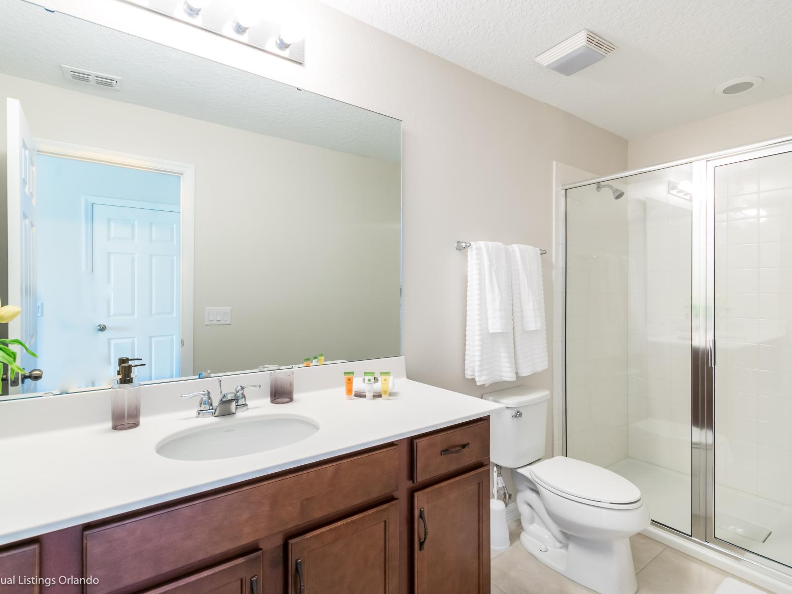 - High-class Bathroom of the apartment in Kissimmee - Beautiful Vanity with large size wall mirror - Sufficient storage space - Neat and clean toilet seat - Availability of all bathroom amenities - Stunning glass cabin shower area