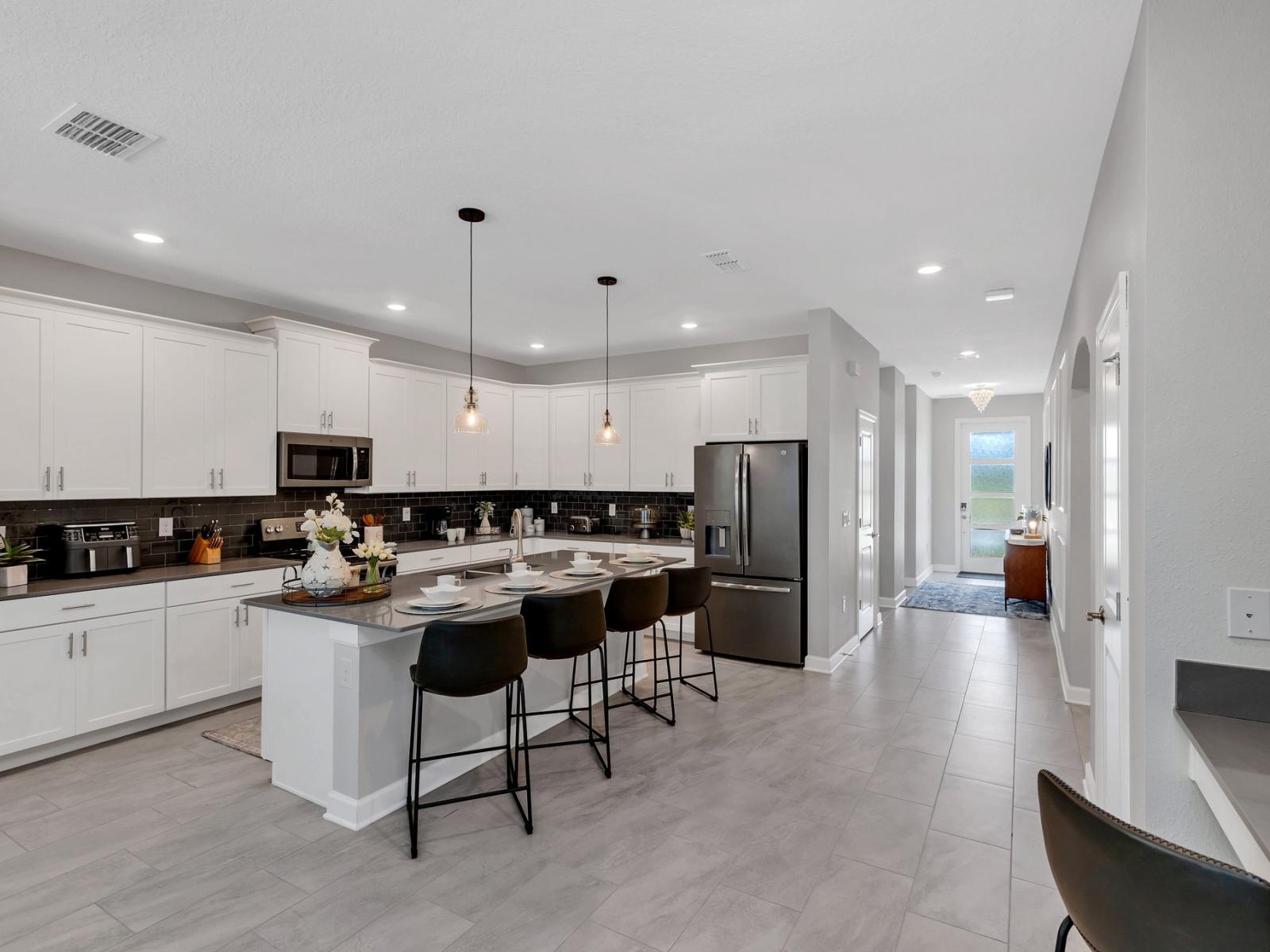 Modern kitchen of the home in Kissimmee Florida - Sleek, stainless steel appliances - Thoughtful placement of kitchen essentials for easy access - Breakfast bar and high chairs - Chic backsplash adding a touch of personality to the space