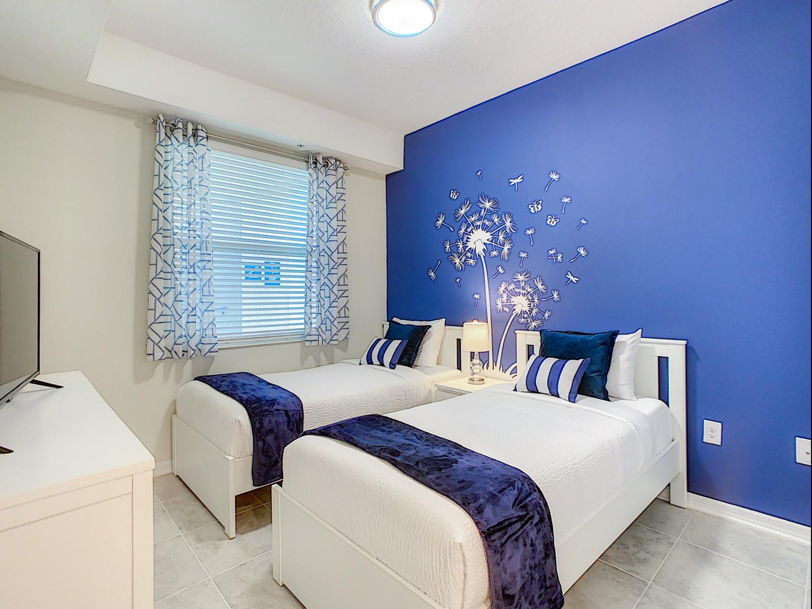 Vibrant, cheerful bedroom featuring a bold blue accent wall and delightful decor - Twin beds with plush linens create the perfect retreat for kids sharing the space - Dandelion wall art brings a touch of whimsy, adding character to this cozy room