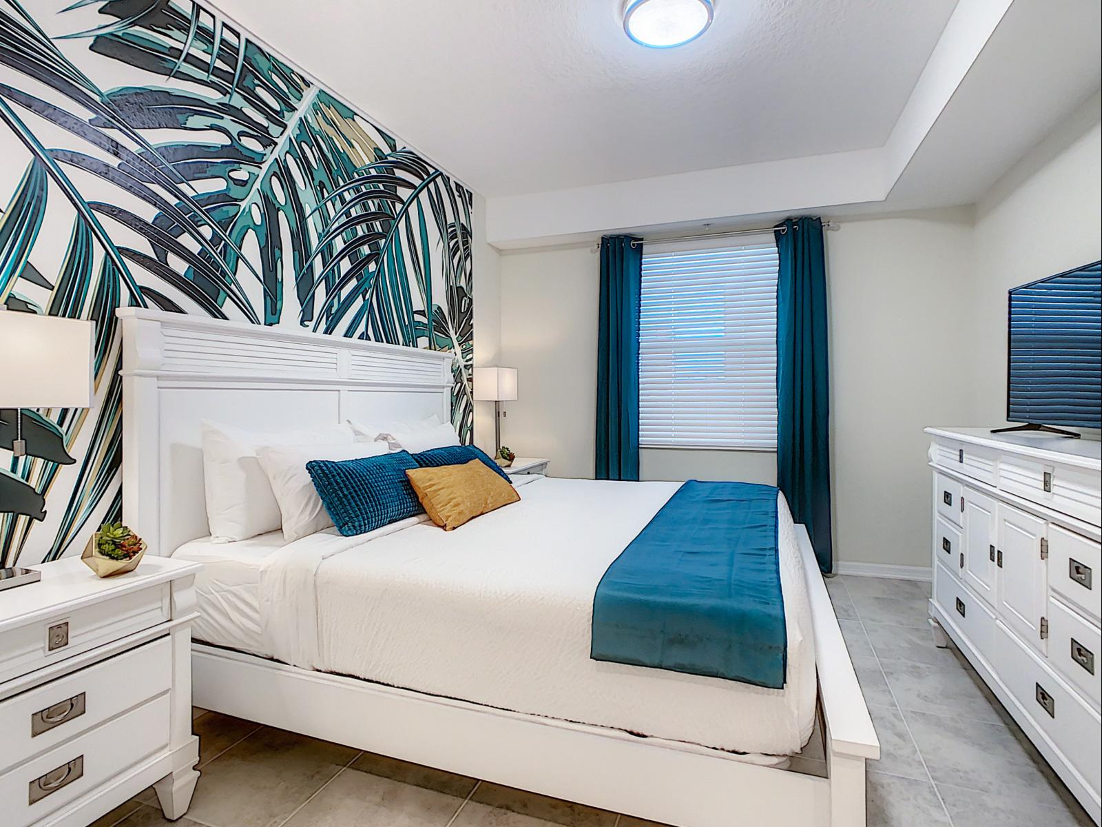 Tropical-inspired bedroom with vibrant palm-print wallpaper that brings the outdoors in - Soft bedding and rich teal accents create a relaxing haven for restful nights - Room’s decor adds an energizing pop, making it as refreshing as it is cozy