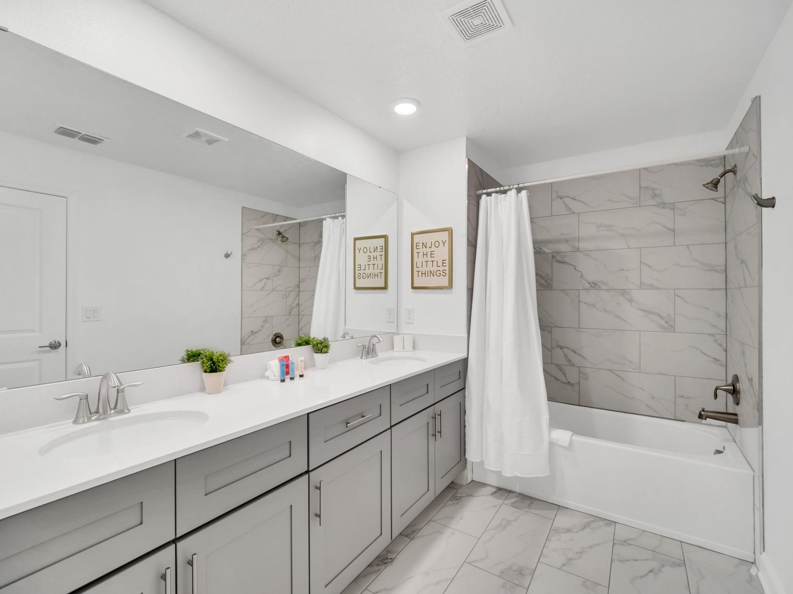 Spacious bathroom of the townhouse in Kissimmee Florida - Luxe dual vanity with large mirror - Features a bathtub and shower combo - Elegant bathroom with luxurious fixtures and finishes