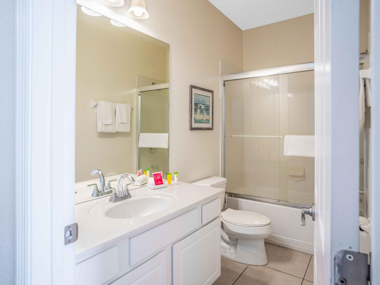 Exclusive bathroom of the townhouse in Orlando - Glorious vanity completed with a big size wall mirror and wall lamp - Neat and clean toilet seat - Fresh towels and all bathroom amenities available - Stunning glass enclosed shower and bathtub combo