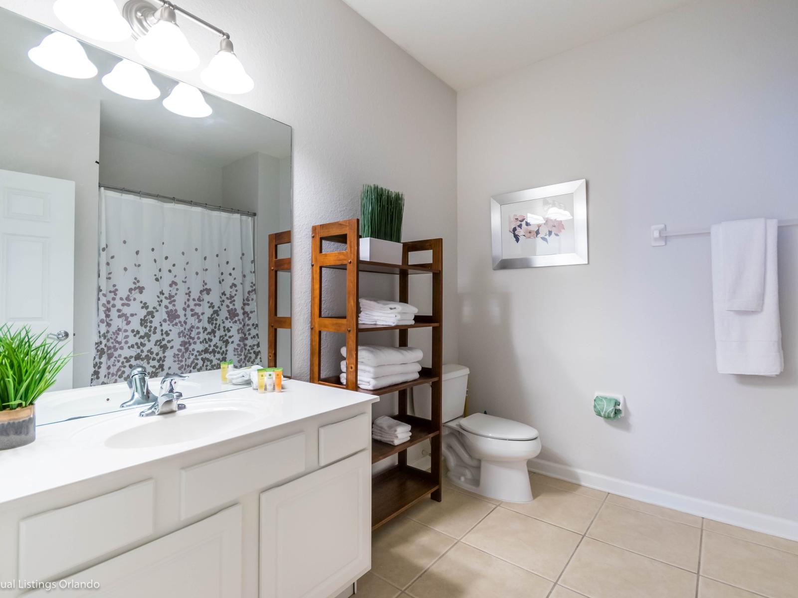 Polished bathroom of the condo in Orlando Florida - Sophisticated color palette creating a serene ambiance - Chic design featuring a sleek vanity and upscale lighting - Thoughtful storage solutions with stylish shelves