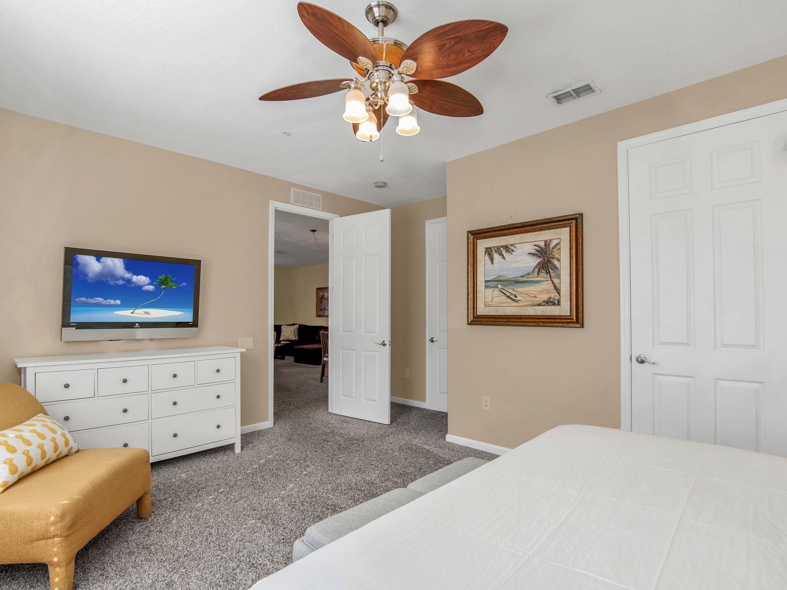 Unwind in this cozy bedroom adorned with an accent chair and a ceiling fan, offering both comfort and style.