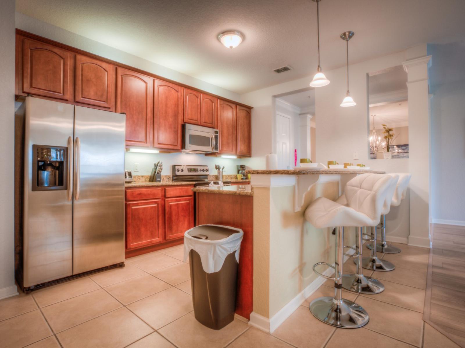 Indulge in our warm-colored kitchen of the condo in Orlando - Complete with a convenient counter table with high chairs - Elegant lighting throughout the space - Plenty of storage space - Fully equipped with all kitchen accessories