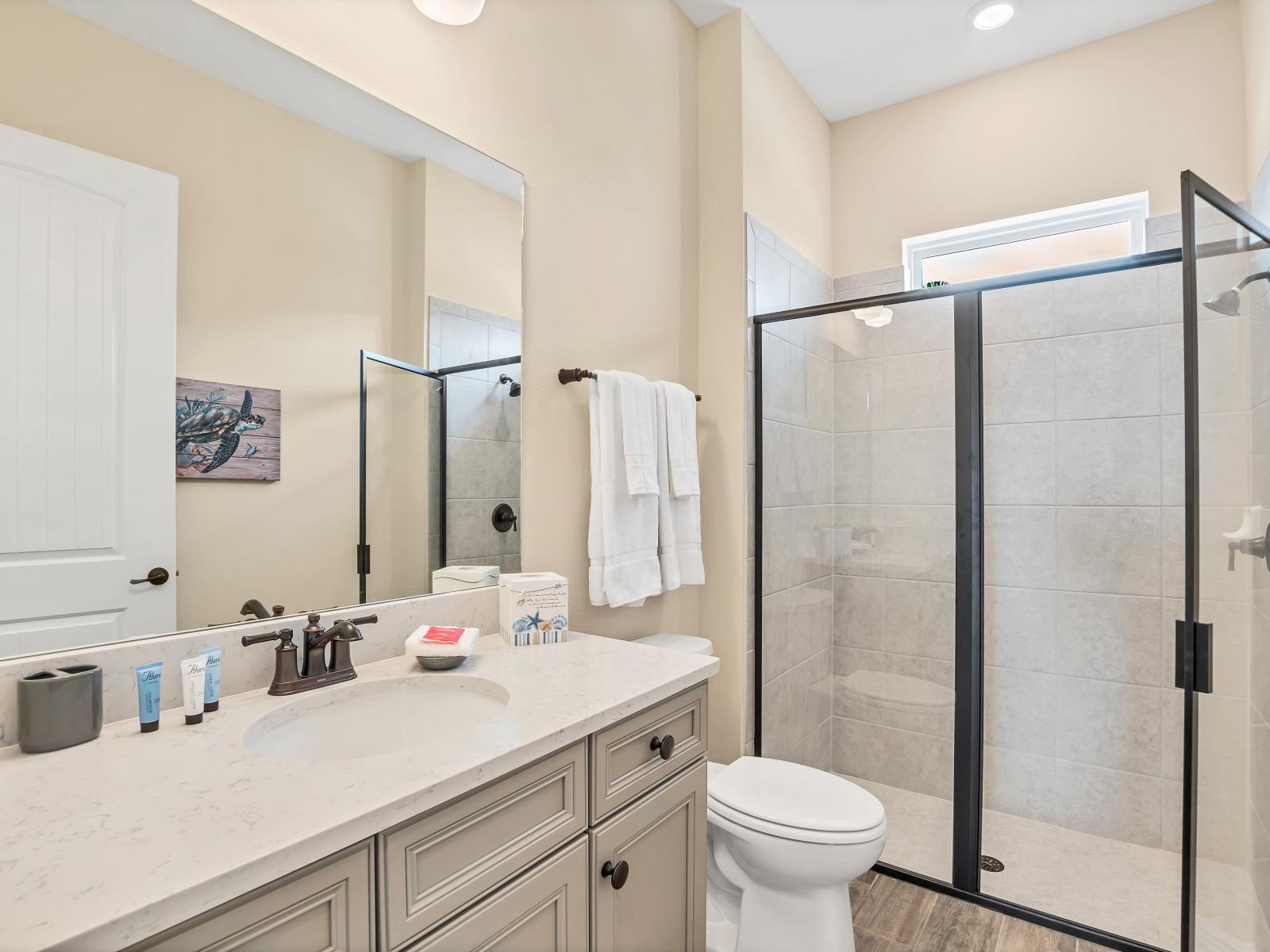 Polished bathroom of the cottage in Florida - Glass-enclosed tiled walk-in shower area - Chic design featuring a sleek vanity and upscale lighting - Contemporary fixtures for a touch of indulgence - Inviting bathroom with a soothing color palette