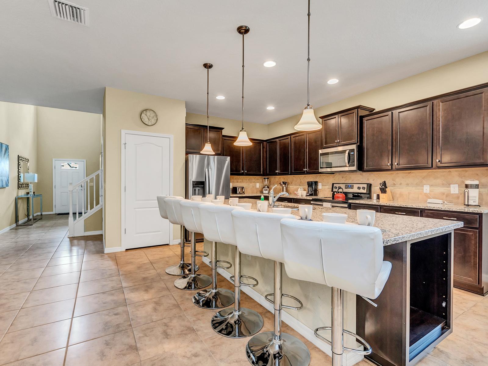 The kitchen adorned with wooden cabinets and a counter bar table exudes rustic elegance, blending natural charm with modern functionality for a warm and inviting culinary space.