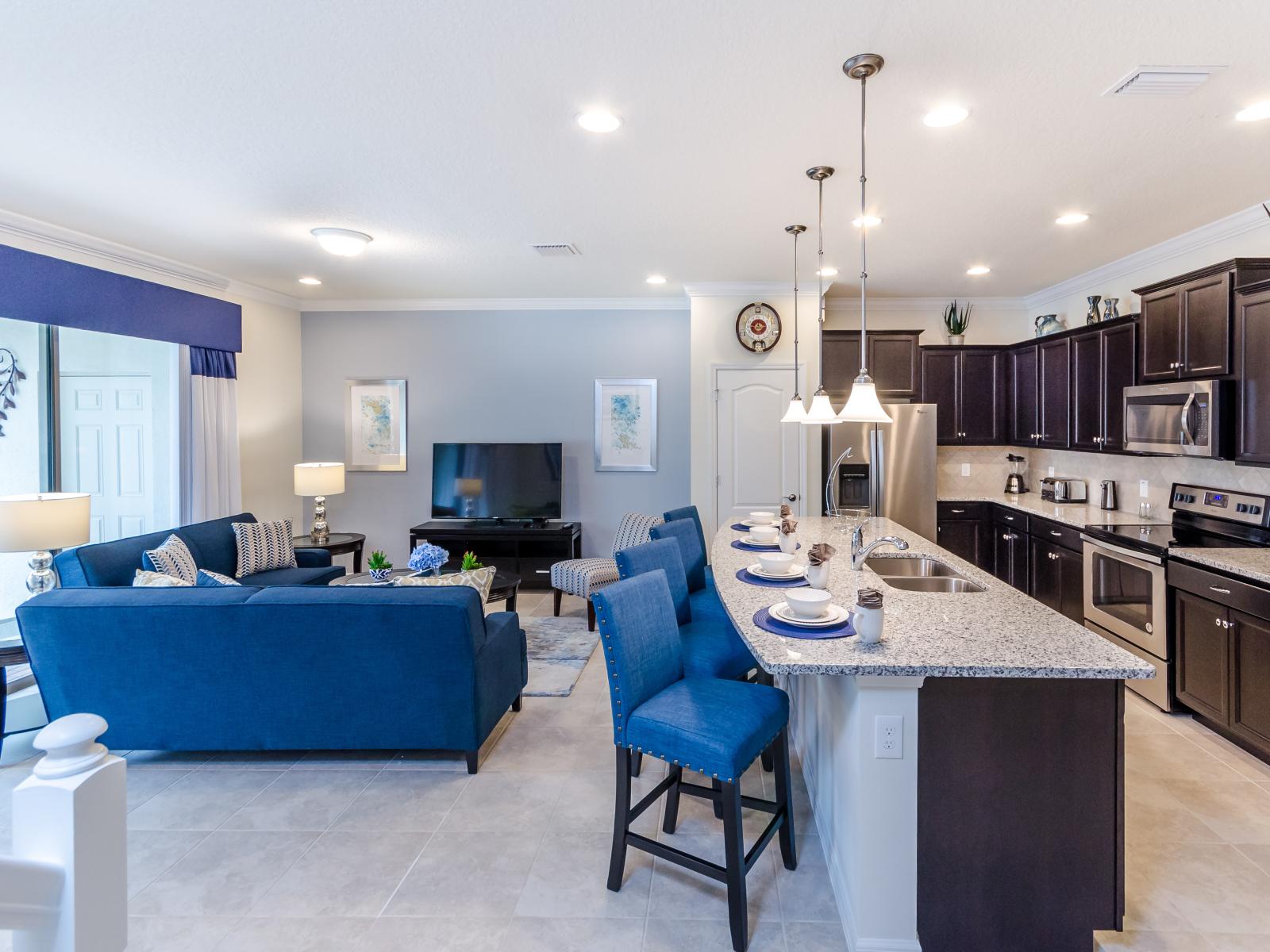 Relax in our spacious living area adorned with a soothing blue-tone couch, seamlessly connected to a fully equipped kitchen area. It's a tranquil retreat where comfort meets functionality, promising moments of relaxation and culinary delight.