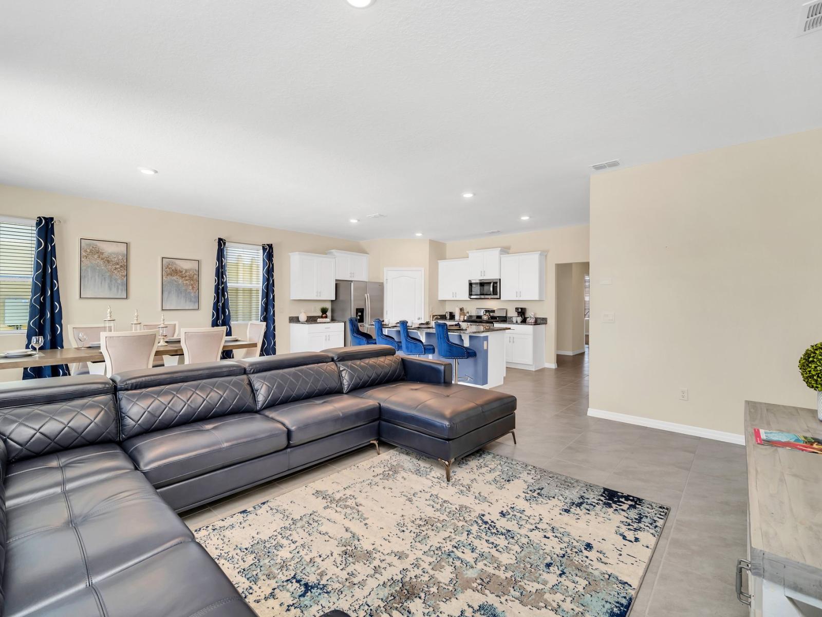 This cozy and sophisticated living room features a leather, wraparound sectional (and built-in chaise lounge), area rug with oceanic undertones, and wall-mounted flat-screen TV.