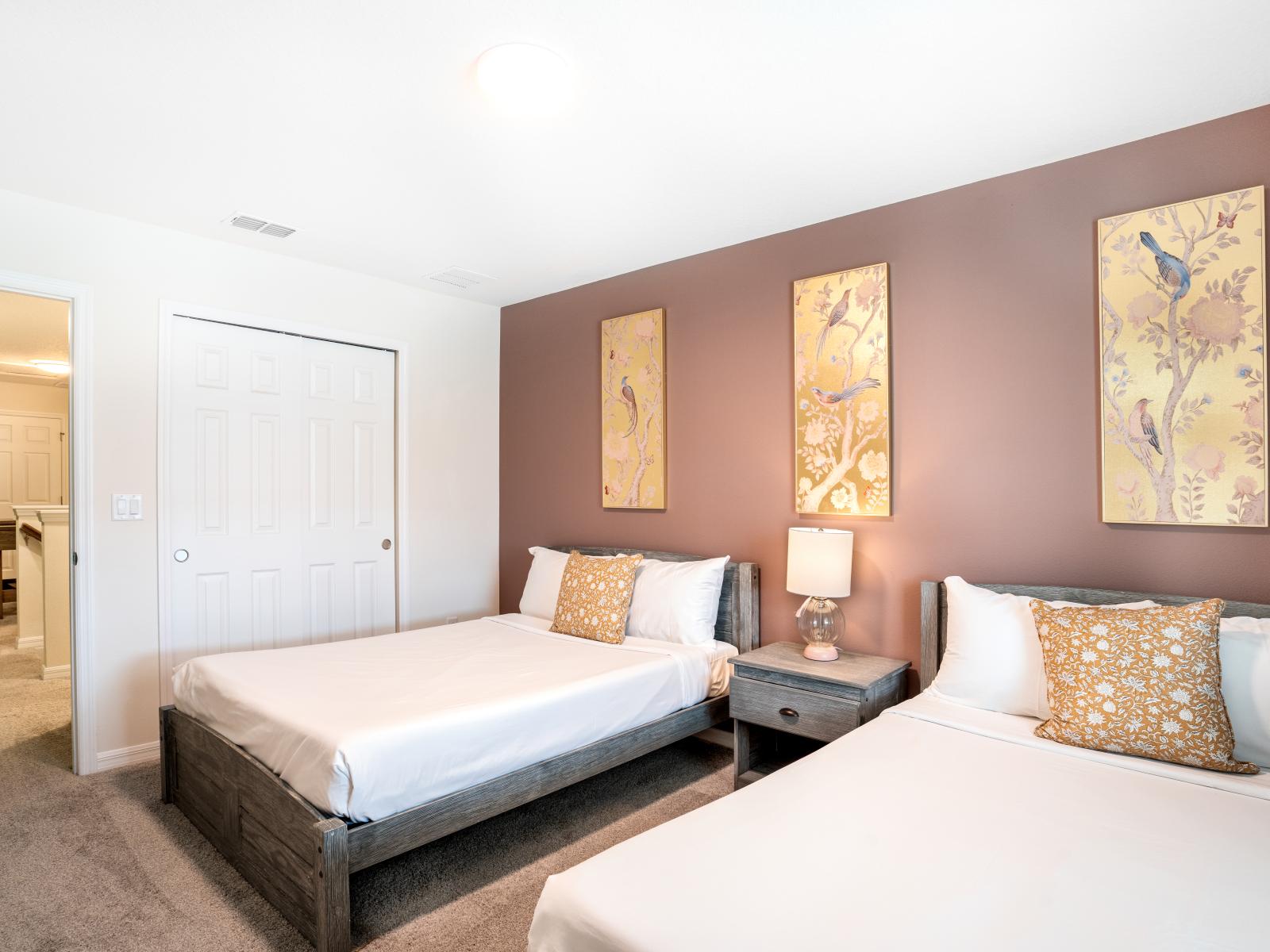 The fifth bedroom showcases 2 full beds, a wall-mounted flat-screen television, shared dresser, and nature-inspired gold leafing artwork upon a tranquil mauve wall.