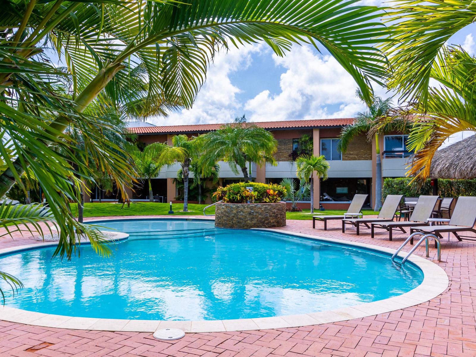 Refreshing tropical Pool Area of the 3BR Condo in Oranjestad Aruba - Relax by the shimmering poolside oasis - Comfort at its best - Enjoy leisurely moments in inviting pool area - Palm trees and tropical plants enhance the vacation feel