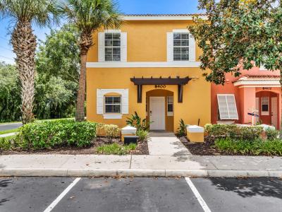 Charming townhouse with a bright yellow facade and white accents, creating a welcoming exterior - Nestled among tall palm trees and lush greenery, providing a tropical ambiance - Convenient parking space located directly in front of the entrance