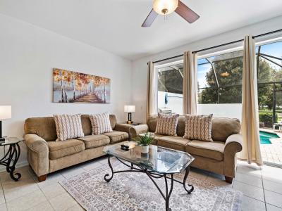 Bright and airy living area with large windows offering a view of the private pool - Comfortable sofas adorned with cushions, creating a cozy atmosphere for relaxation - Elegant glass table and stylish decor elements enhance the inviting ambiance